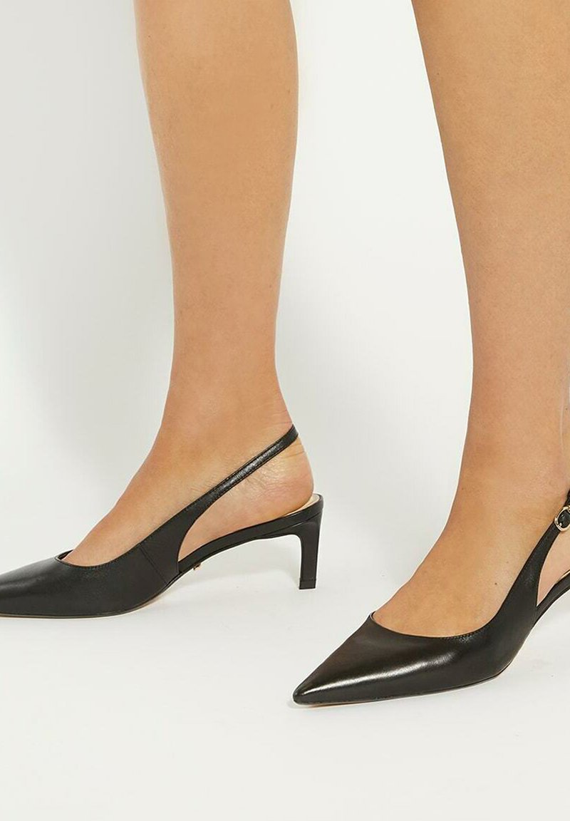 Zwarte leren slingback schoenen met een spitse neus, een lage hak en uitgesneden zijkanten, voorzien van een slanke enkelband en een kleine decoratieve gesp.