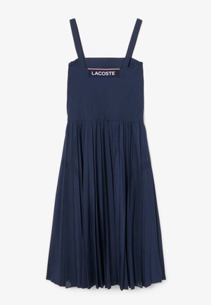Navy blue dress with adjustable thin straps, a fitted bodice, and a pleated skirt featuring mesh panel accents. Lacoste logo at the neckline.