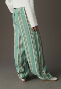 Pantalon léger à rayures vertes avec une ceinture élastique, présentant des rayures verticales blanches et beige, associé à des baskets blanches.