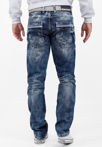 Jeans in denim blu con un lavaggio scolorito, dotati di una vita a media altezza, cinque tasche e tasche posteriori con logo. Abbinati a sneakers bianche.