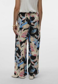 Bloemrijke wijde broek met een zwarte basis en grote roze, blauwe en crème bladerenpatronen. Elastische tailleband, lichte stof.