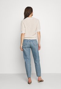 Mujer de espaldas con un suéter de punto de manga corta beige, unos vaqueros de cintura alta azul claro y sandalias de tacón con estampado de animal.