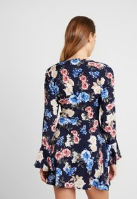 Blommig klänning med långa klockärmar, marinblå bakgrund, med rosa, blå och krämfärgade blommor. Kort längd med en figursydd midja.