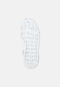 White rubber shoe sole with black speckles, featuring circular grip patterns and ridges for traction. Smooth texture and rounded shape.