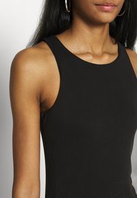 Black ribbed sleeveless top with a round neckline, featuring a smooth texture and fitted design, showcasing the shoulder and neck area.