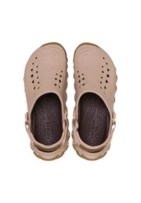 Beige Crocs met een geperforerd ontwerp, verstelbare achterband en een bruine, gestructureerde binnenzool. Lichtgewicht materiaal met een chunky zool.