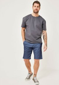 Men's outfit featuring a gray T-shirt with a round neck and navy blue shorts. The shorts have a smooth texture. White and gray sneakers complete the look.