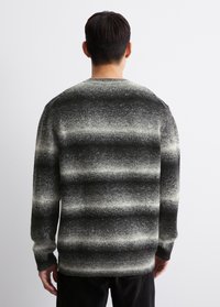 Strickpullover mit Rundhalsausschnitt, der ein Farbverlaufdesign mit abwechselnden schwarz-weißen Streifen aufweist. Strukturierte Oberfläche, lange Ärmel und gerippter Saum.