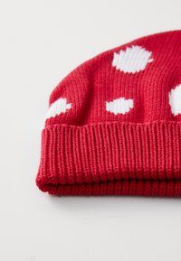 Rote gestrickte Mütze mit weißen Punkten, geripptem Saum, weichem Material und runder Krone. Geeignet für den Winter.