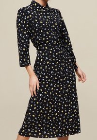 Abito floreale nero con motivi gialli e blu, design con colletto, maniche lunghe, lunghezza media, tessuto leggero e chiusura con bottoni.