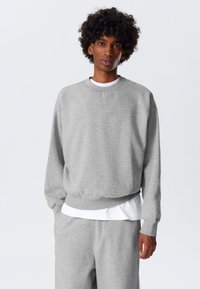 Grijze sweatshirt met lange mouwen, ronde hals en geribbelde boorden. Draagt over een wit shirt, wat een casual en ontspannen uitstraling geeft.