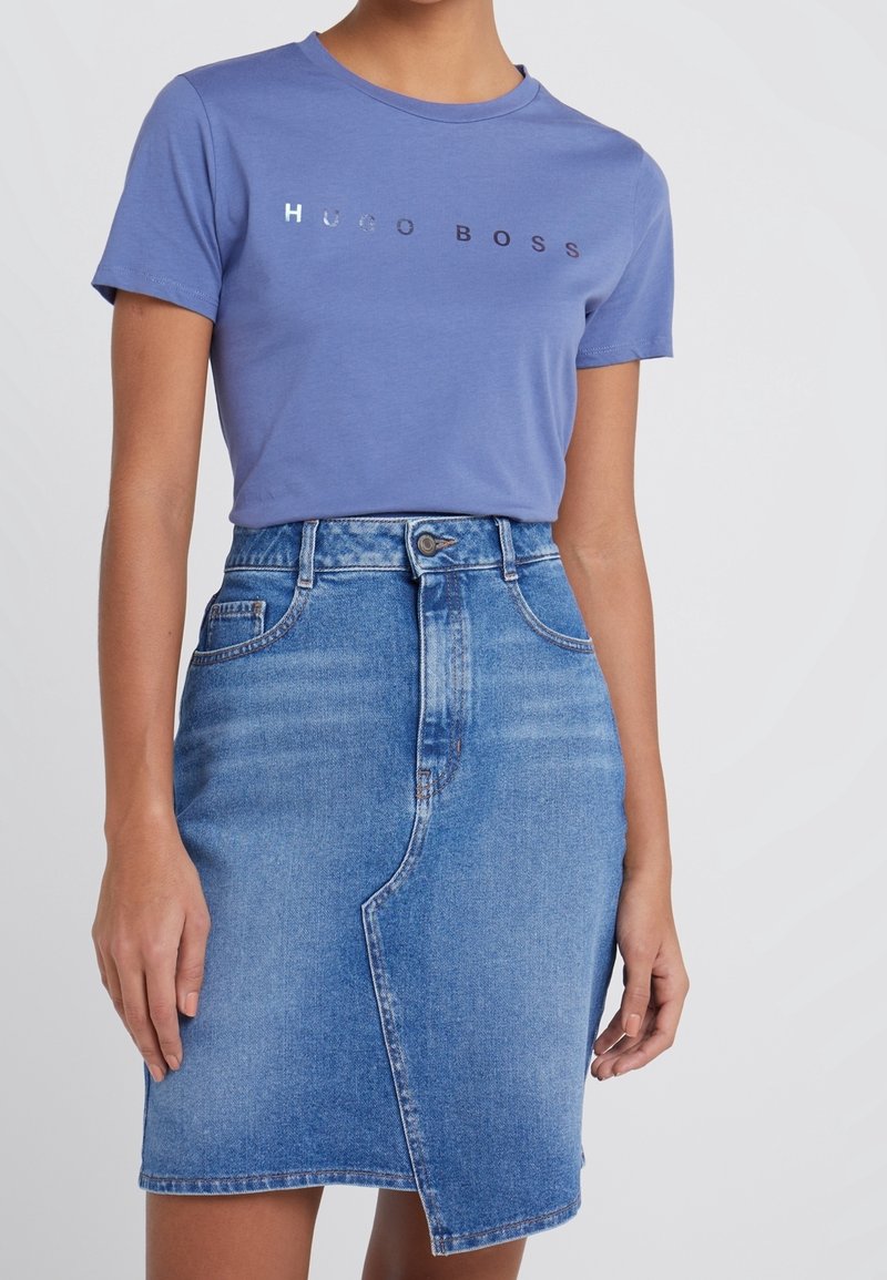 Camiseta de algodón azul con el logo "HUGO BOSS", combinada con una falda lápiz de mezclilla azul claro que presenta una cintura alta y una abertura frontal.