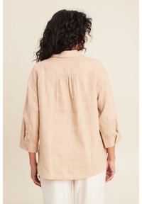Camicia di lino beige con piega sul retro, maniche a tre quarti e polsini con bottoni. Tessuto morbido con una vestibilità rilassata.
