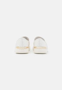 Scarpe bianche senza lacci con un motivo geometrico testurizzato, caratterizzate da una striscia in accento oro e una suola in gomma. Design minimalista con finitura liscia.