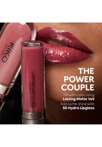 Nærbilde av glansfulle lepper med mørkerød leppestift ved siden av matchende Lasting Matte Veil flytende leppestift og 3D Hydra Lipgloss tuber.