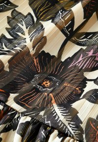Floral fabric featuring large black and orange flowers with yellow and green accents on a cream background. Pleated texture at the bottom.