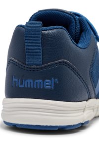 Zapatilla deportiva azul con parte superior de cuero texturizado y malla, suela blanca y una pequeña tira de agarre. Presenta el logotipo "hummel" en azul en el lateral.