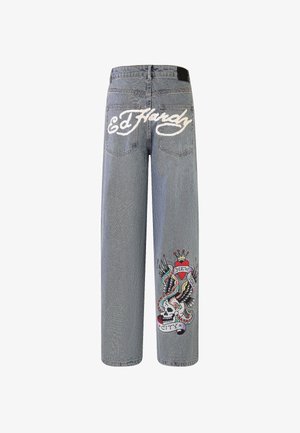 Lyseblå jeans med "Ed Hardy"-logo på baglommerne og farverigt tatoveringsstilmotiv med kranium, slange og hjerte på det nederste højre ben.