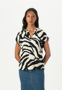 Blouse à manches courtes avec un motif zèbre noir et blanc. Tissu léger avec un col en V et des manches retroussées, associée à une jupe en denim.