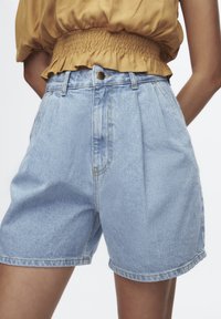 Pantalones cortos de mezclilla azul claro con cintura alta, diseño plisado y cierre frontal con botones. Presentan costuras sutiles y un ajuste relajado.