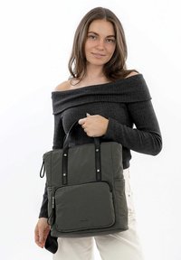 Sac en toile vert avec poignées noires, fermeture zippée et poche frontale. Texture lisse avec des accents de couture subtils.