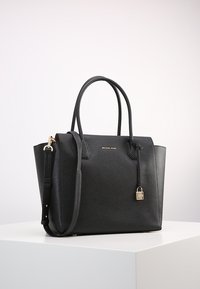 Sac fourre-tout en cuir noir au design structuré, avec deux poignées, une bandoulière amovible, des accessoires en or et un petit détail de cadenas.