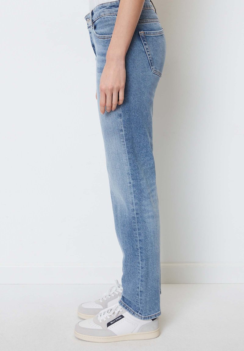 Helle blaue Jeans aus Denim mit geradem Schnitt, mittlerer Bundhöhe und dezenten Abnutzungserscheinungen. Kombiniert mit weißen und grauen Turnschuhen.