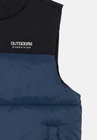 Pufasta prsluk u mornarskoplavoj i crnoj boji, napravljen od izoliranog materijala. Na prsima sadrži vezene natpise "OUTDOORS" i "Expedition". Standardni kroj i dizajn.