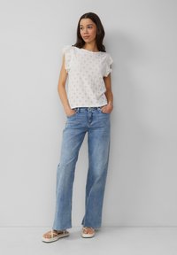 Weißes Spitzenoberteil mit Rüschensäumen, kombiniert mit hellblauen weit geschnittenen Jeans und flachen Sandalen. Sauberes Design mit lässiger Passform.