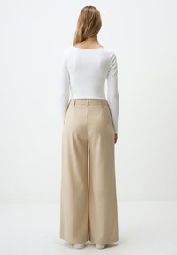 Witte geribde langwerpige top gecombineerd met hoge beige wijde broek, met een gladde stof en nette taillebanddetail.