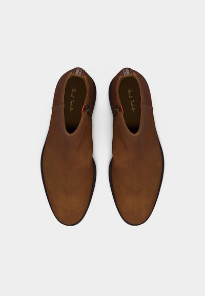 Paire de chaussures en daim marron à enfiler avec des languettes multicolores en tissu et des semelles noires, vues de dessus sur fond blanc.