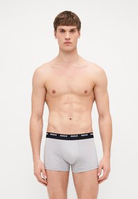Graue Baumwoll-Boxershorts mit einem schwarzen Elastikbund, der den Markennamen "HUGO" in weißen Buchstaben trägt. Glattes, eng anliegendes Design.