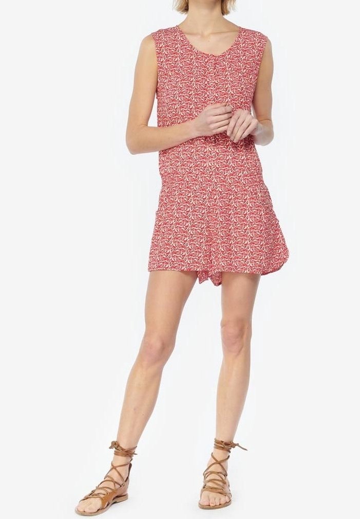 Femme portant une robe rouge sans manches à motif floral et des sandales camel à lacets, debout devant un fond blanc uni.