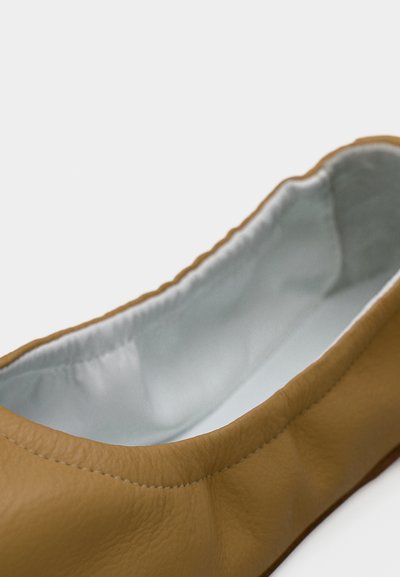 Κοντινό ενός μπαλέτου μπαλαρίνας από ταμπά δέρμα που δείχνει μαλακή, ανοιχτό γκρι εσωτερική επένδυση και ραμμένη άνω άκρη.