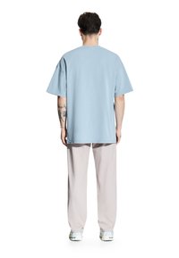 Jasnoniebieska, oversize koszulka z krótkim rękawem, okrągłym dekoltem i miękkim bawełnianym materiałem, zestawiona z jasnobeżowymi spodniami i sportowymi butami.