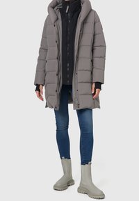 Grå puffjakke med hætte og quiltet design lagdelt over en sort zip-up jakke. Sammen med blå jeans og lysegrå ankelstøvler.