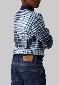 Maglione a quadri blu e navy con colletto a coste, abbinato a jeans scuri con etichetta beige di Calvin Klein Jeans nella vita.
