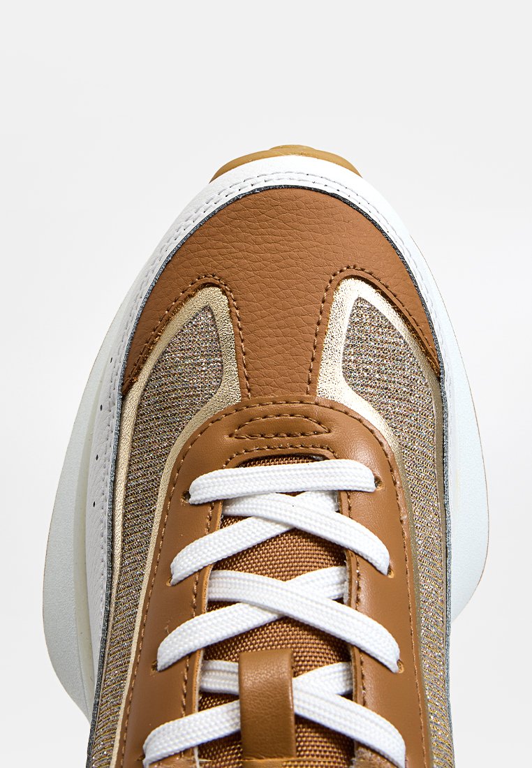 Basket en cuir marron avec accents dorés, sections en tissu texturé, lacets blancs et semelle en caoutchouc blanc ; vue en gros plan.