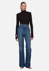 Modré džínsy s vysokým pásom a širokými nohavicami, spárované s čiernym rolákom s dlhým rukávom. Vyznačujú sa hladkým materiálom a priliehavým strihom.