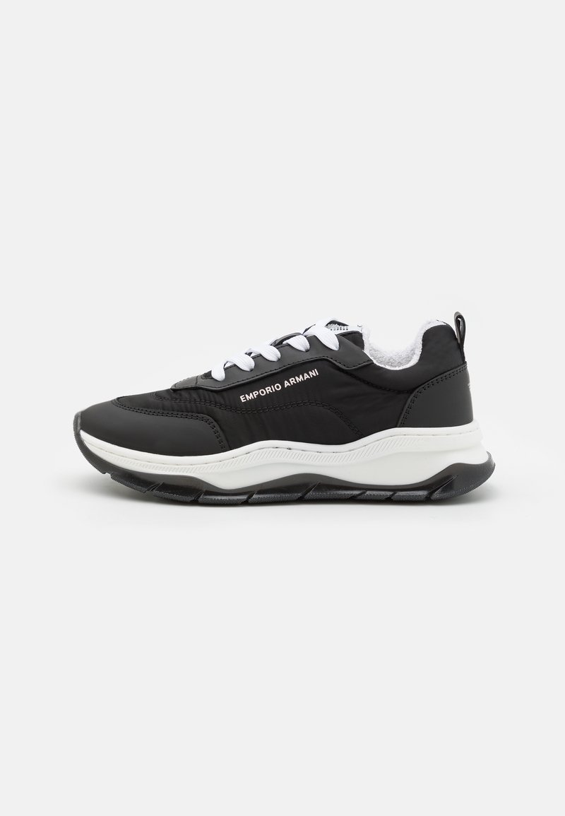 Baskets Emporio Armani noires et blanches avec semelle épaisse, lacets blancs et détail latéral marqué sur un fond uni.