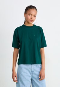 Grønn bomulls t-skjorte med korte ermer, rund hals og en liten logo på brystet, kombinert med lyseblå denimbukser.