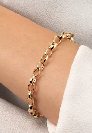 Goldkette-Armband mit großen ovalen Gliedern, getragen am Handgelenk vor hellem Stoffhintergrund.