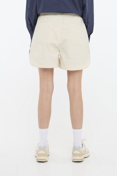 Lys beige shorts med en teksturert finish, med en elastisk midje og to baklommer, sammen med en navy stor skjorte.