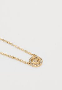 Collier en chaîne dorée avec un pendentif en spirale orné de strass clairs le long du bord extérieur. Texture métallique lisse, design circulaire.