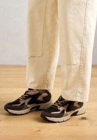 Sneakers with a black mesh upper, tan and brown suede accents, and beige rubber sole; feature textured leopard print detail.