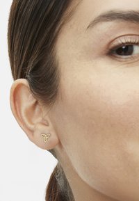 Guld postøreringe i et minimalistisk design, der har tre sammenkoblede bladformer, præsenteret på en øreflip med glat hud.