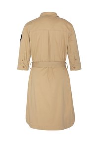 Abito camicia beige, con lunghezza fino al ginocchio, colletto, maniche a tre quarti, vita elastica e una cintura coordinata. Include una toppa sulla manica sinistra.