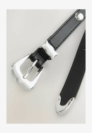 Crna kožna remen sa sjajnom srebrnom metalnom kopčom i akcentom u obliku zvijezde. Remen se odlikuje glatkom teksturom i šiljastim krajevima s metalnim vrhovima.