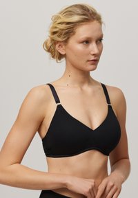 Bralette triangular negro hecho de tela suave, con tirantes ajustables y un borde decorativo con volantes en la parte inferior.