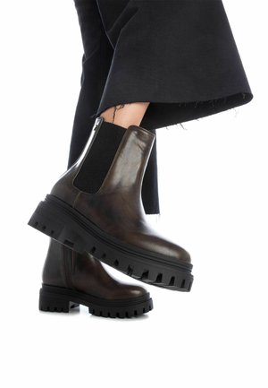 Stivali alla caviglia in pelle marrone con pannello laterale elastico texturizzato, suola nera in gomma spessa e zip laterale. Abbinati a pantaloni neri a sbalzo.